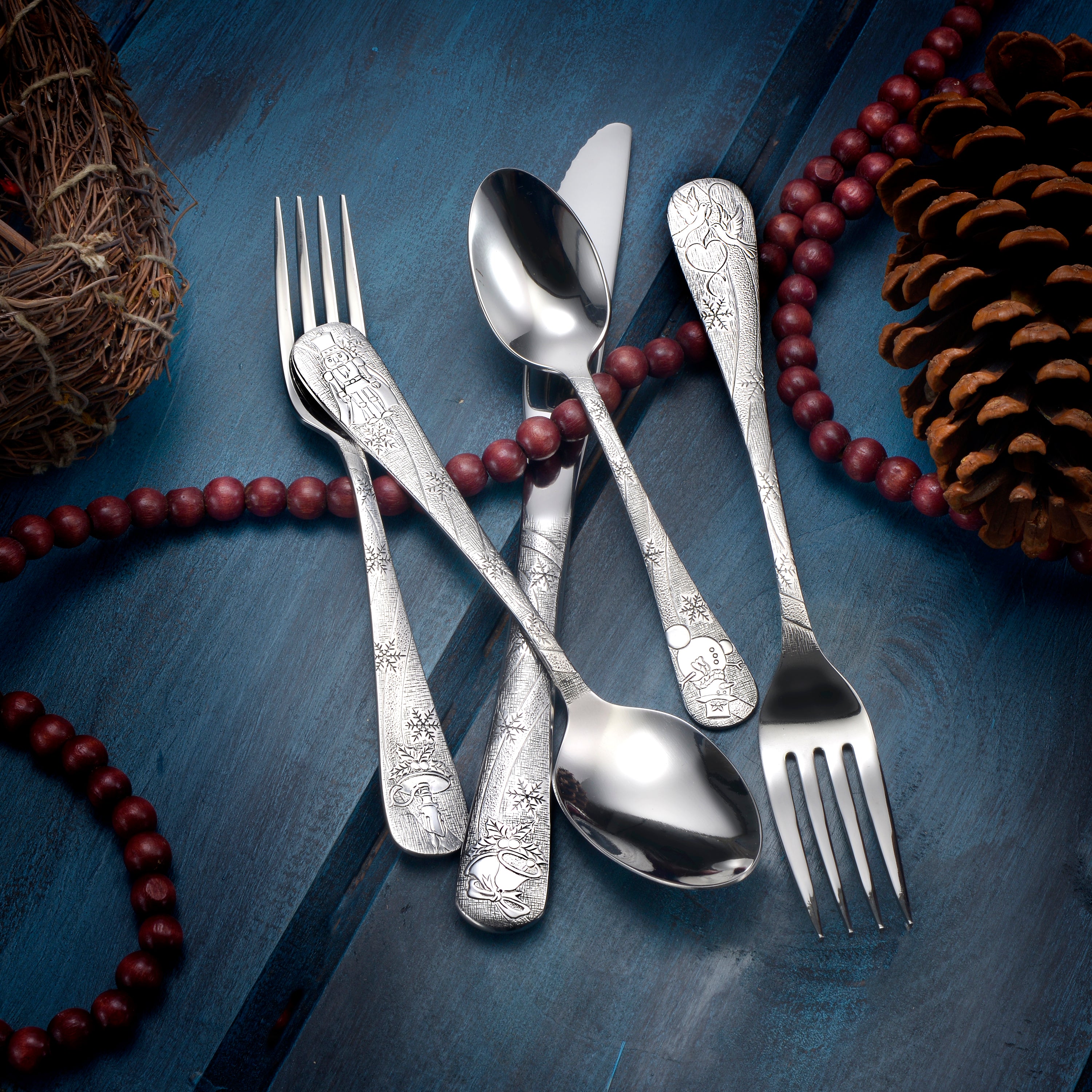 Five pieces of decorative flatware with intricate designs on handles, arranged on a blue wooden surface with holiday decor.