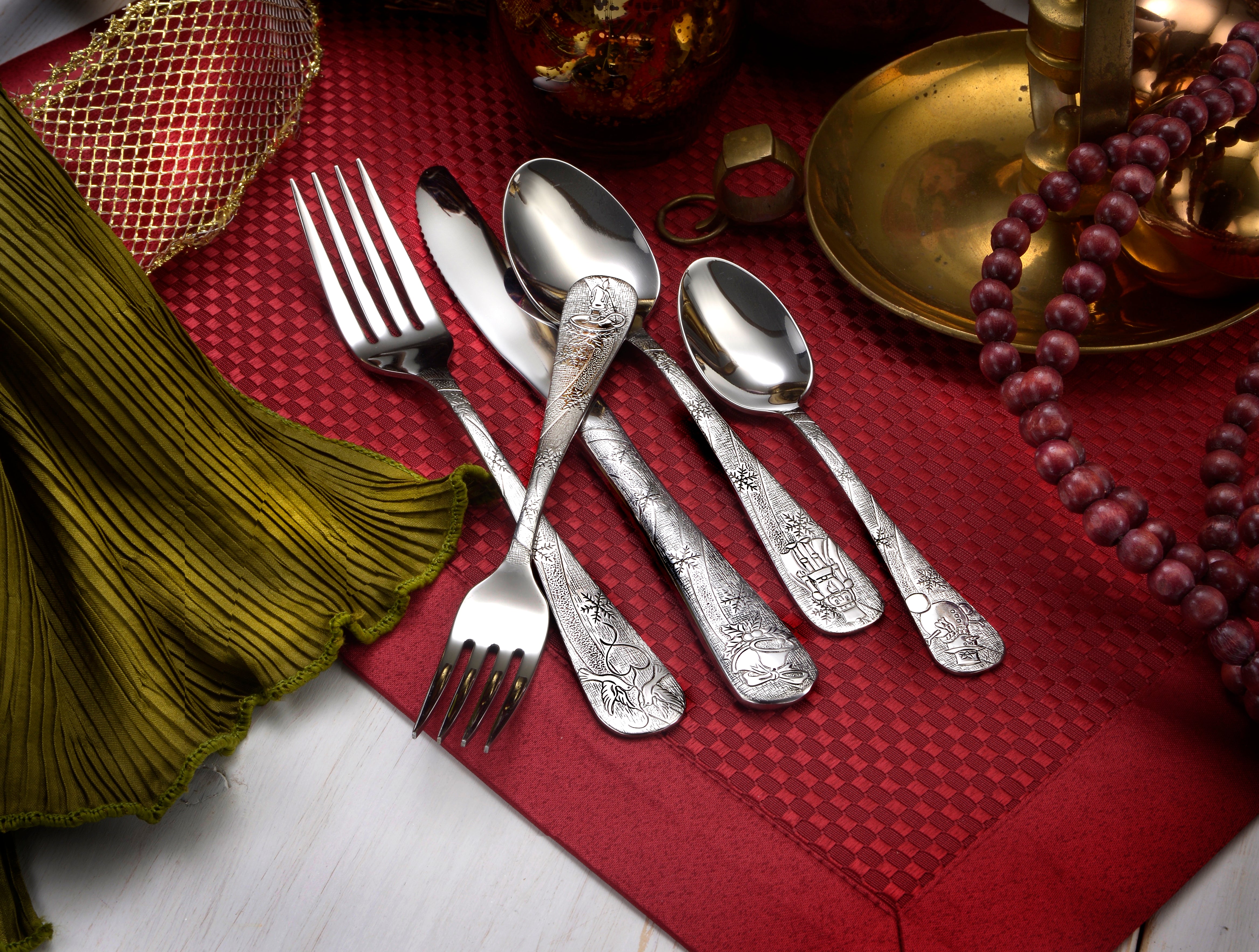 Five pieces of ornate flatware on a festive table setting with a red background.