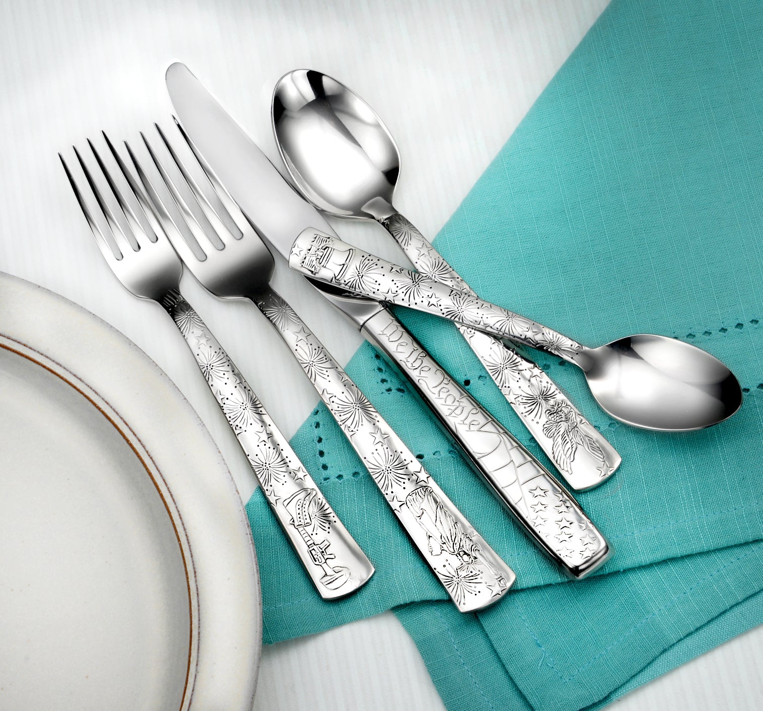 Liberty- 65 Piece Set featuring intricate designs on utensils, displayed on a teal napkin and plate