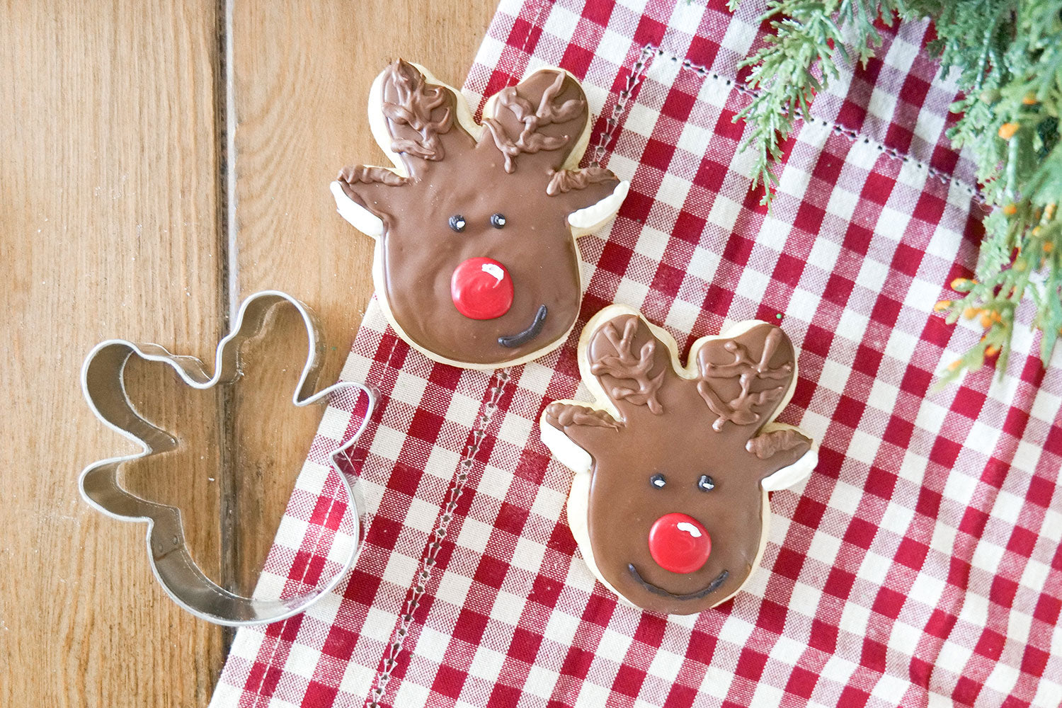 Reindeer head cookie cutter next to decorated reindeer cookies on a checkered cloth
