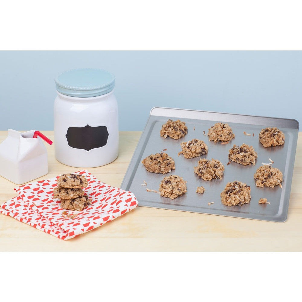 A medium stainless steel cookie sheet with cookies on it, next to a jar and a napkin.