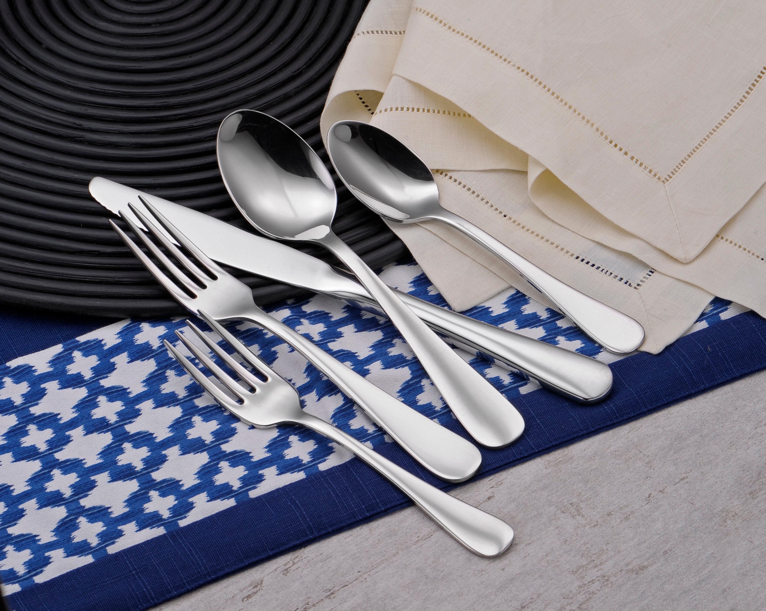 A set of stainless steel flatware including forks, knives, and spoons arranged on a table setting.