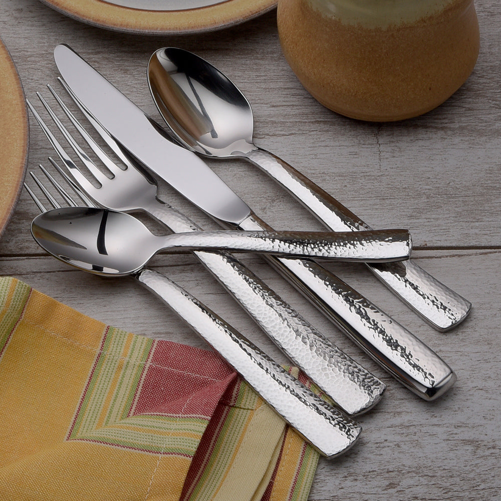 Pinehurst 65 Piece Flatware Set displayed on a table with plates and a napkin