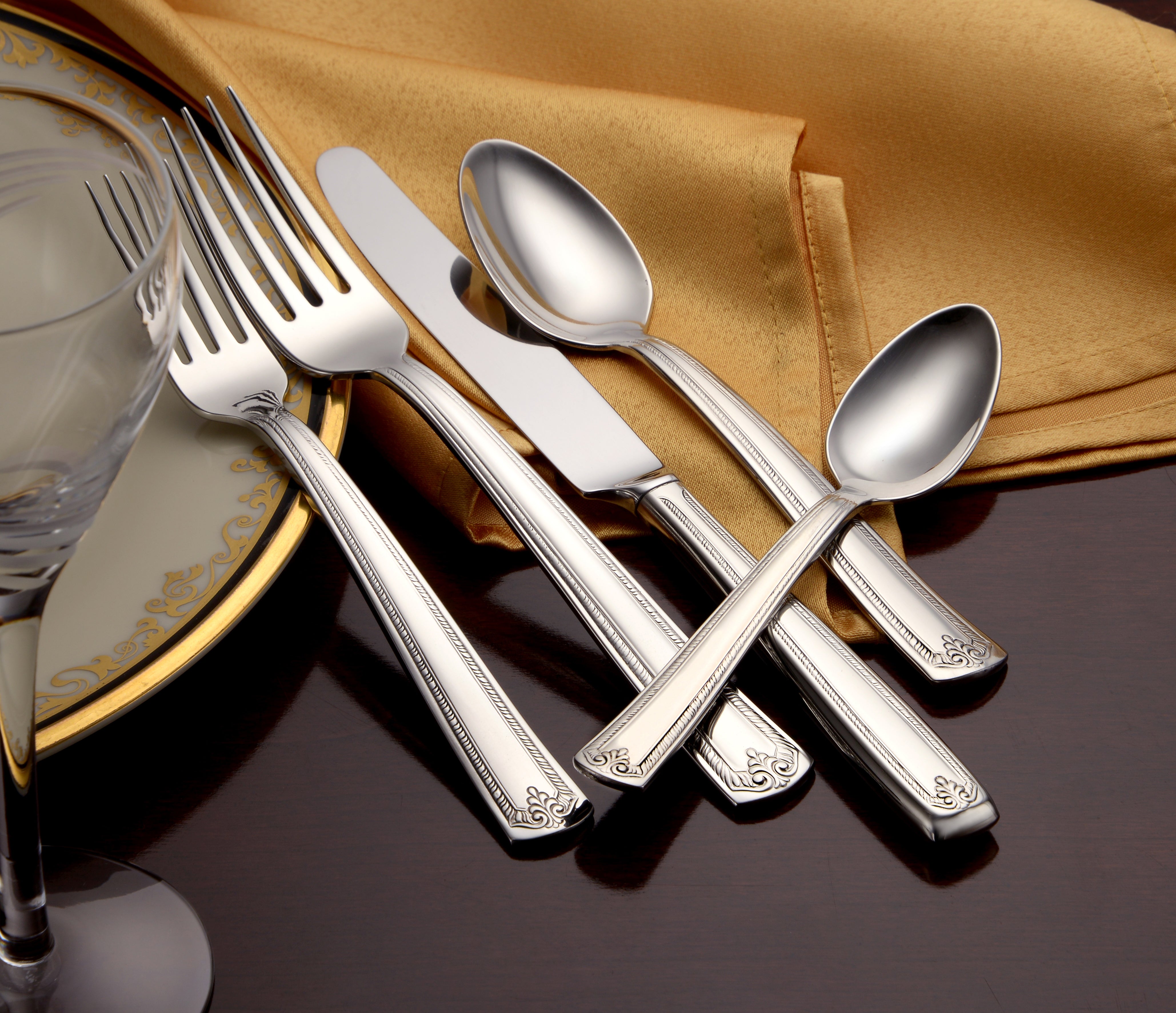 A close-up of Prestige 65 Piece flatware set on a table with a gold tablecloth.