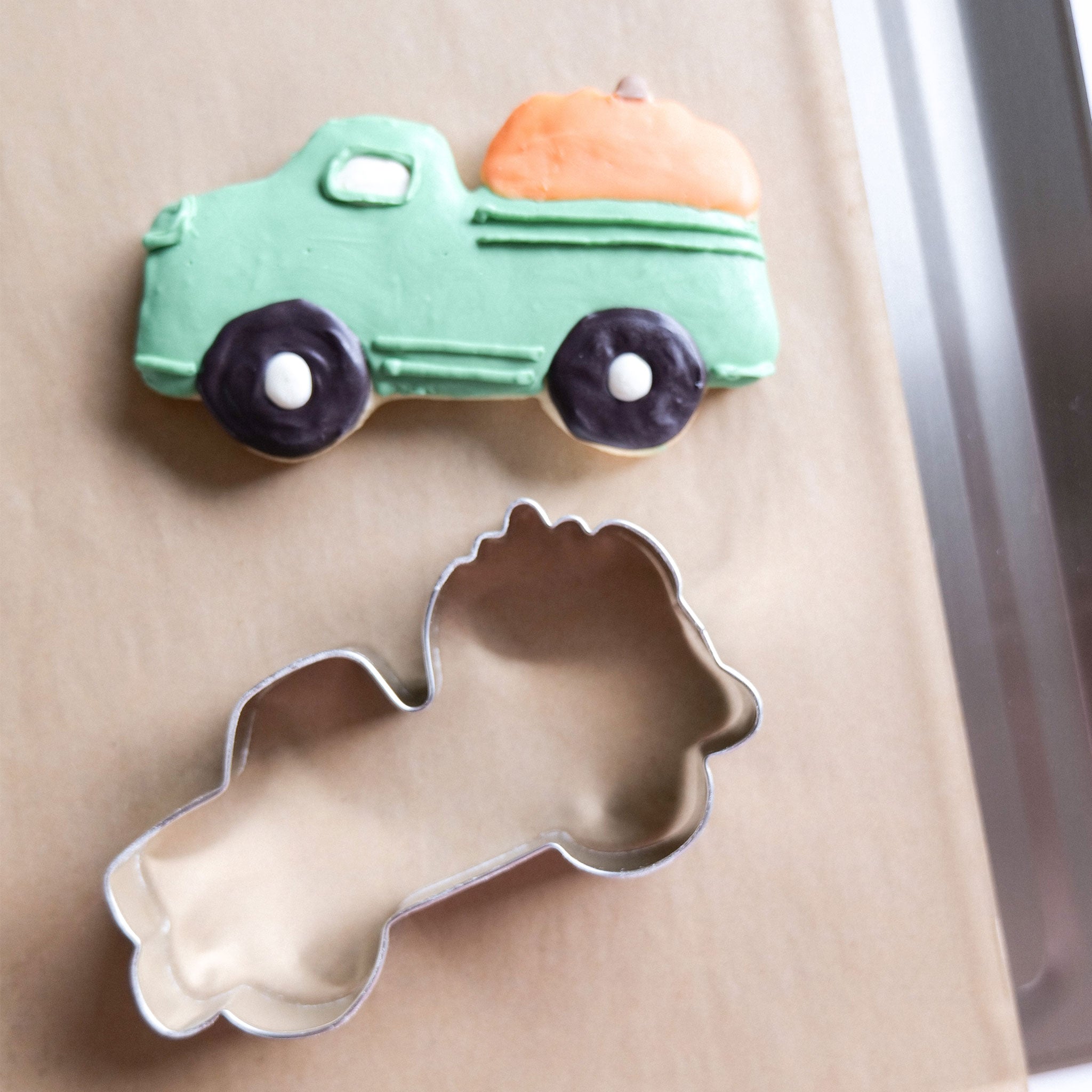 A green truck-shaped cookie with an orange pumpkin on top and a metal cookie cutter in the shape of a truck.