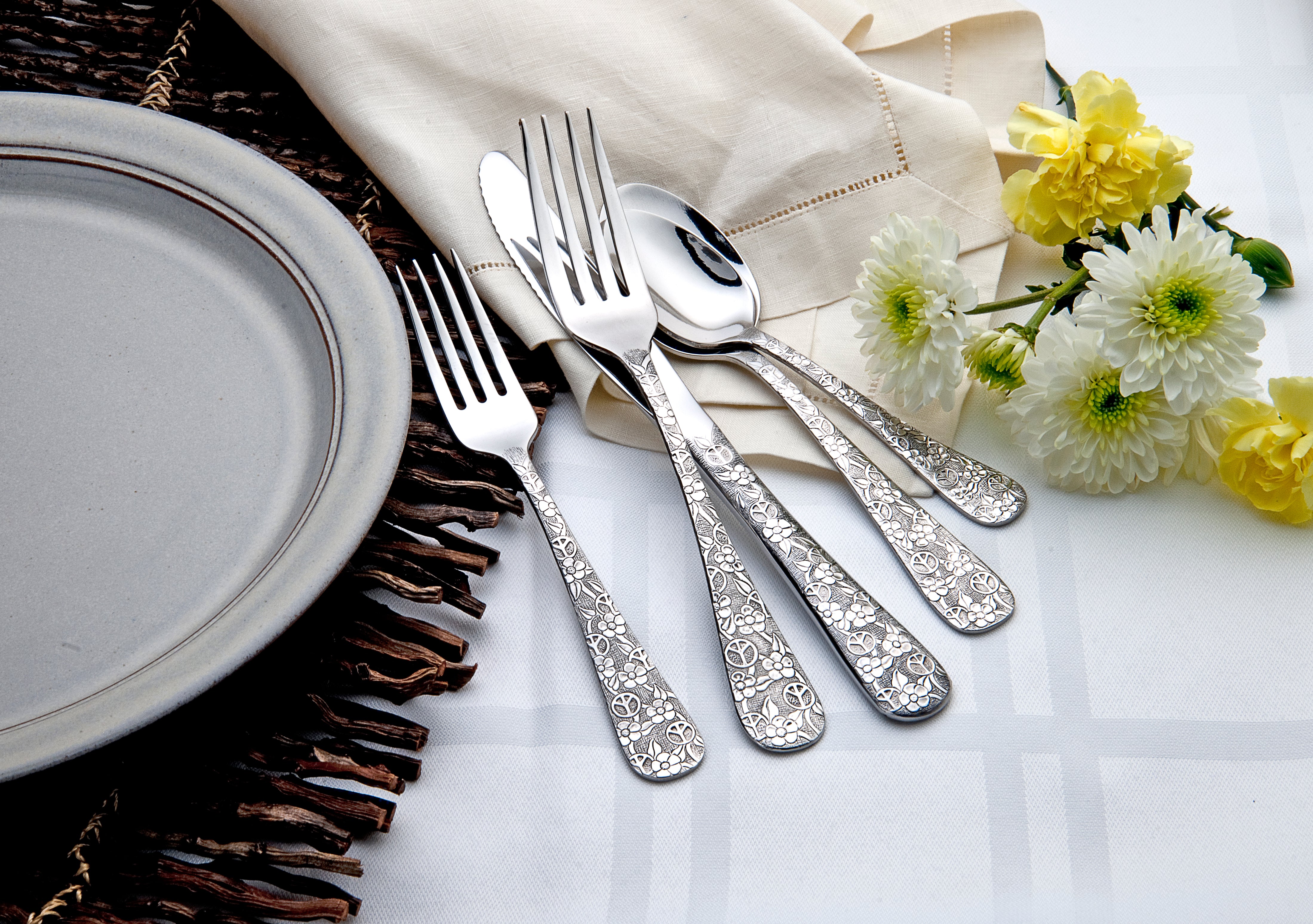Four pieces of Woodstock flatware on a table with a plate and flowers