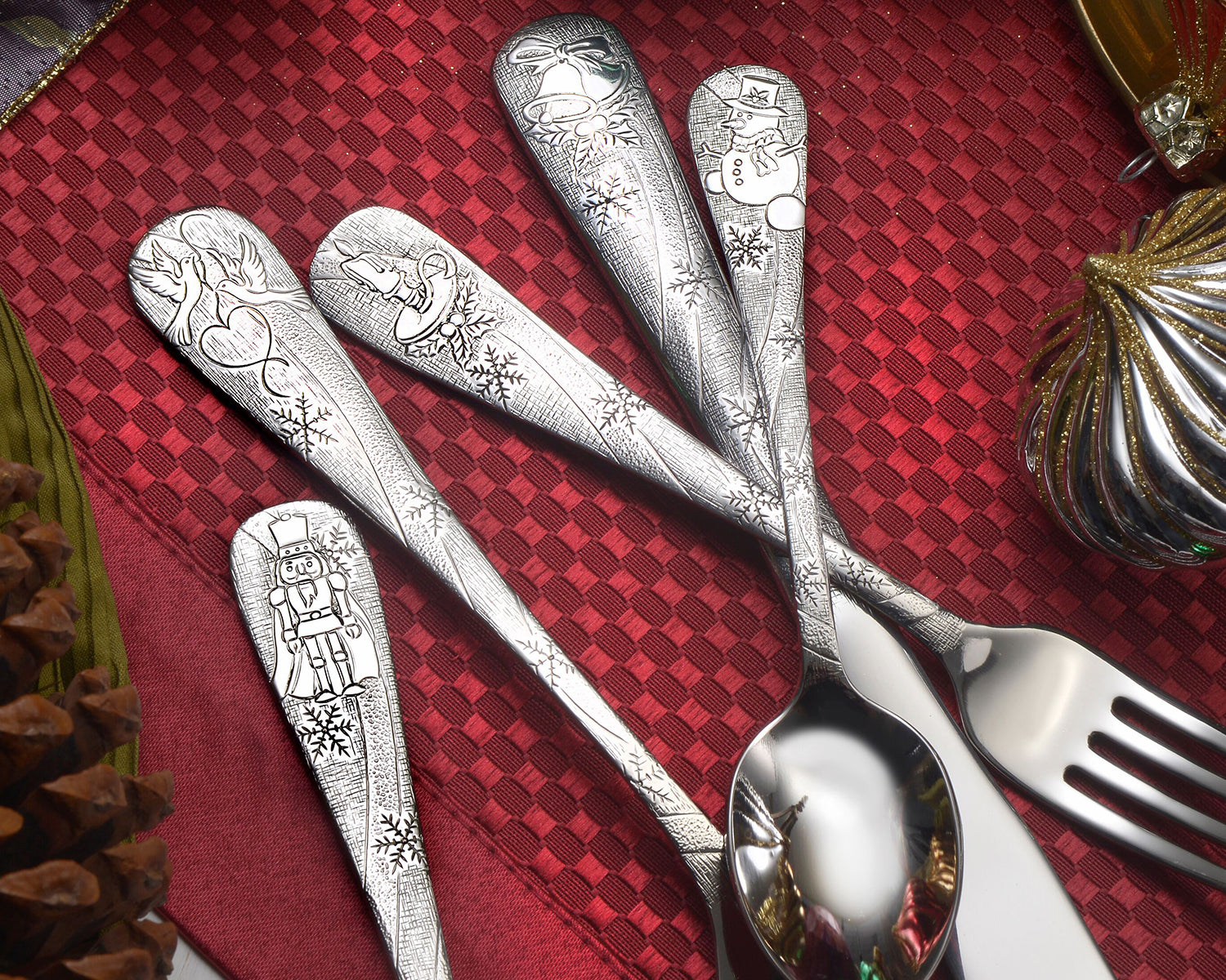 Four pieces of engraved holiday-themed flatware on a red tablecloth