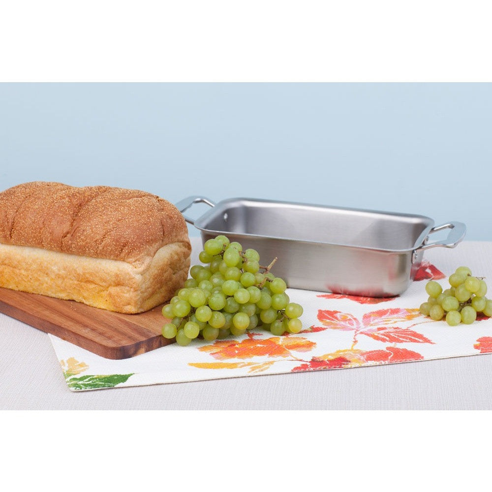 Stainless steel loaf pan with bread and grapes on a table