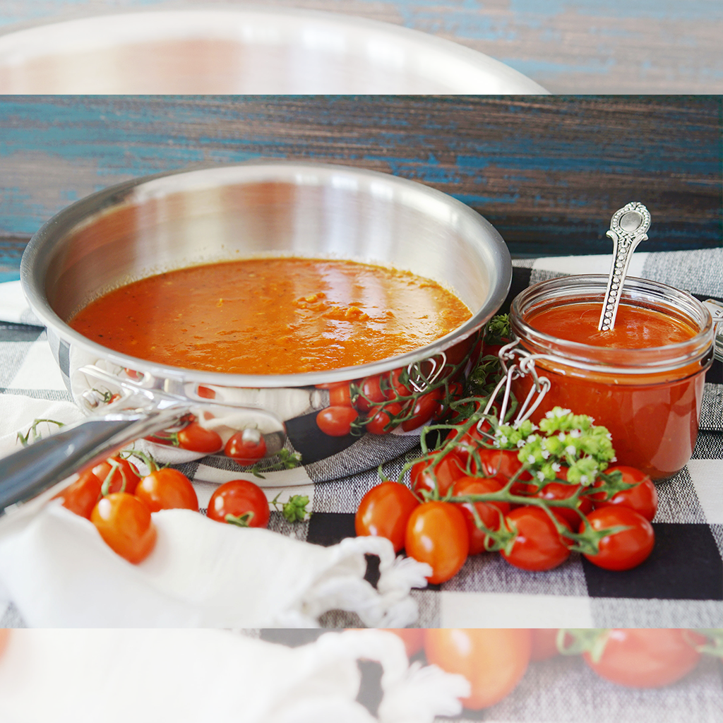A 2-quart stainless steel saucier with tomato sauce and fresh tomatoes on a checkered cloth.